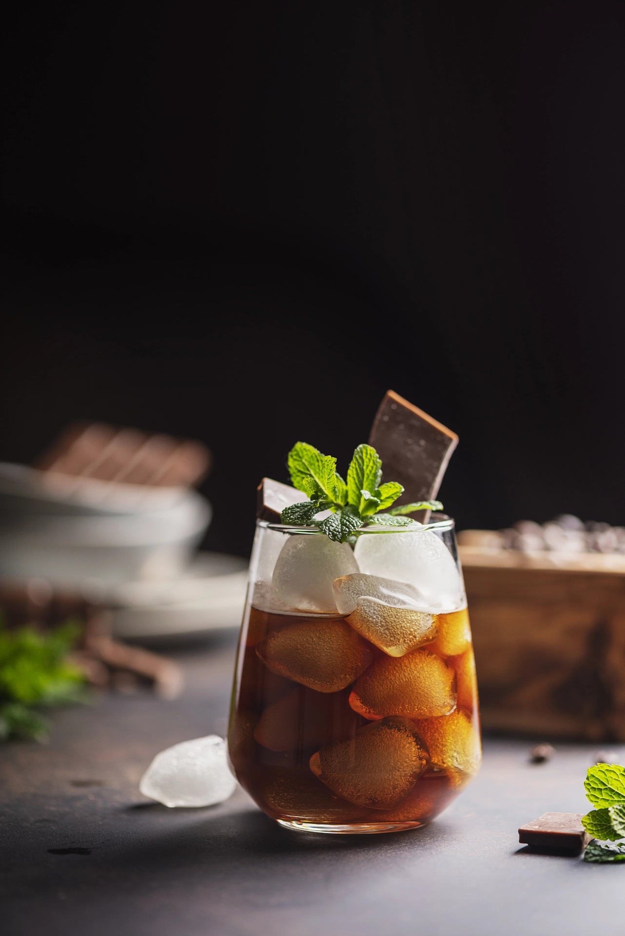 Vaso de mazagrán con hielo, hojas de menta y una rodaja de chocolate, fondo oscuro