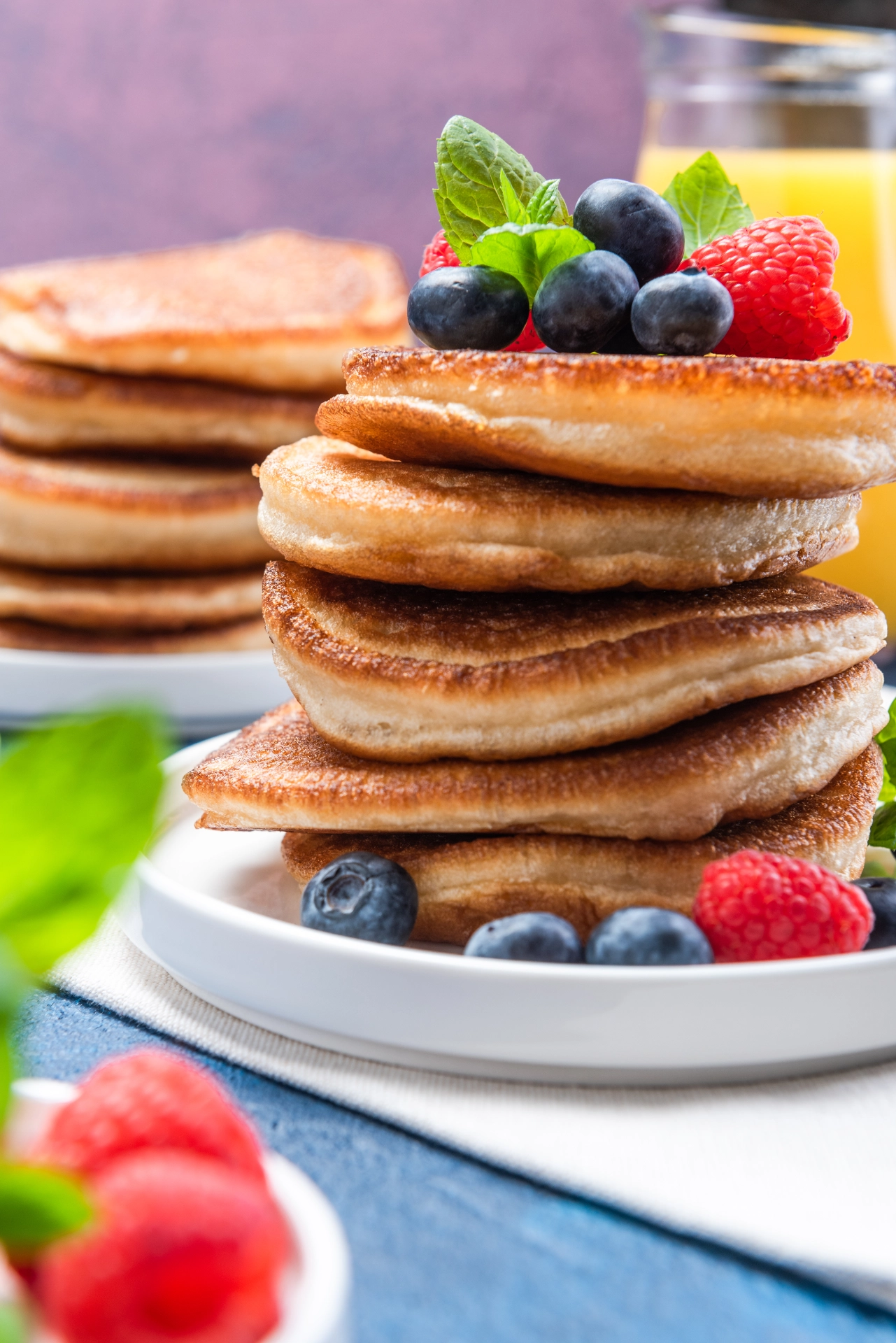 Pila de pancakes dorados con frambuesas, arándanos y hojas de menta encima
